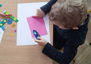 Chlopiec samodzielnie komponuje robota, przyklejając papierowe elementy