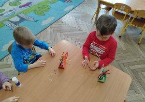 dzieci siedzą przy stolikach i wykonują prace plastyczne.