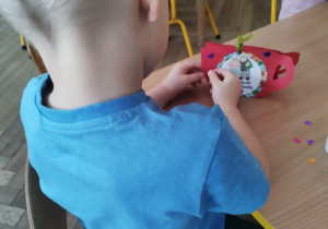 Chlopiec wykonuje prace plastyczną ozdabia kubeczek serduszkami