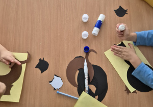 Dzieci siedzą przy stole i sklejają poszczególne części kota w całość.