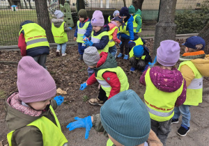 Dzieci są ubrane w kamizelki odblaskowe. Dzieci przychylają się i podnoszą śmieci.