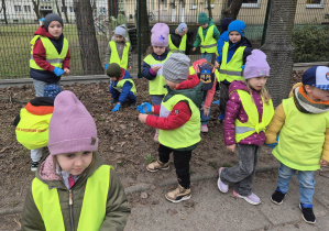 Dzieci ubrane w kamizelki odblaskowe porządkują teren wokół przedszkola.