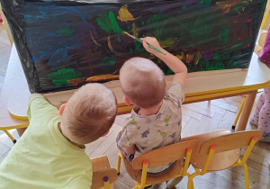 Chłopiec siedzi na krześle i maluje wiosnę drugi chłopie się przygląda