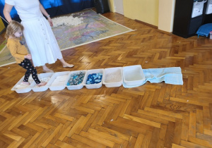 Pani prowadzi dziewczynkę przez ścieżkę sensoryczną.