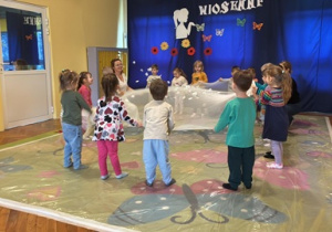 Dzieci podrzucają piórka na foli malarskiej.