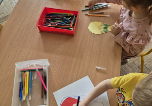 Dzieci malują laurki, kolorują serce kredkami.