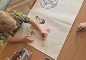Chłopiec maluje kredkami na dużym kartonie.