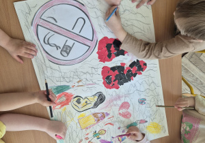 Dzieci malują kredkami plakat. Wyklejają kawałkami kolorowego papieru sylwetę płuc. Dzieci rysują swoje elementy wymyślone przez nich samych.