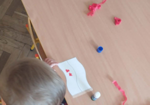 Dzieci siedzą przy stolikach i biorą udział w zajęciach plastycznych tworzą swoje flagi