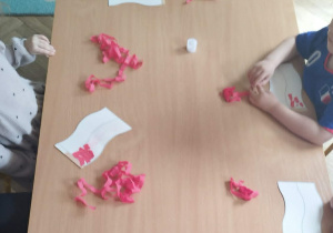 Dzieci siedzą przy stolikach i biorą udział w zajęciach plastycznych tworzą swoje flagi