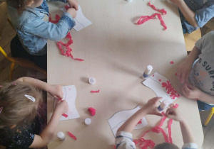 Dzieci siedzą przy stolikach i biorą udział w zajęciach plastycznych tworzą swoje flagi