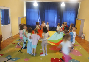 Dzieci na dywanie bawią się chustą animacyjna i na krążkach