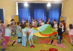 Dzieci na dywanie bawią się chustą animacyjna i na krążkach