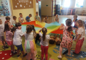 Dzieci na dywanie bawią się chustą animacyjna i na krążkach