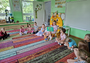 Dzieci siedzą na dywanie w kole i słuchają koleżanki