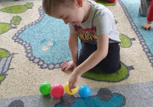 chłopiec na dywanie układa piłki